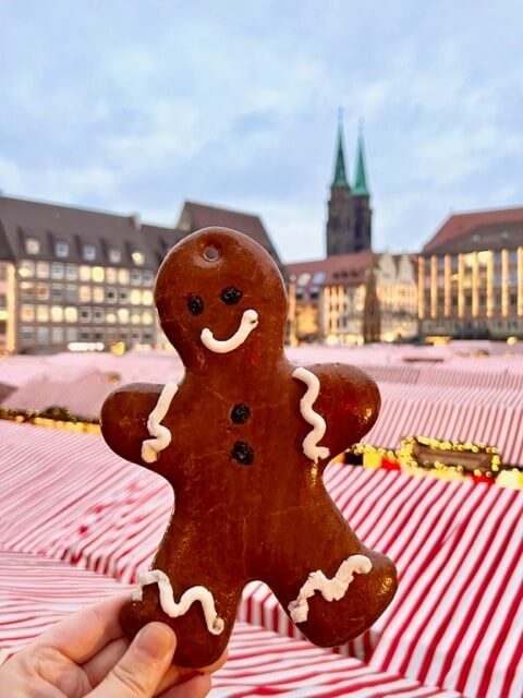 A decorated gingerbread man is held aloft over the red and white striped tents of the Christkindlesmarkt in Nuremberg, showing how to visit Nuremberg in winter