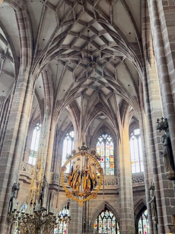 Soaring columns and stained glass windows make up the inside of the Lorenzkirche in Nuremberg, a large carving hangs from the ceiling showing angelic figures