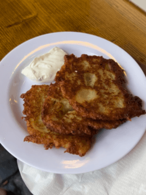 Two potato fritters sit on a white plate with a creamy dipping sauce