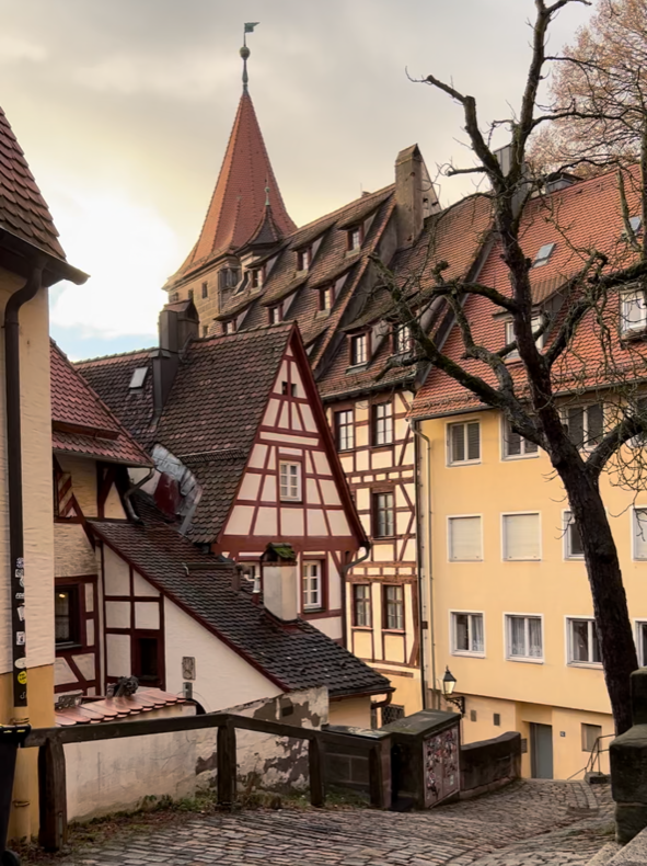 Half timbered houses are nestled into a cosy laneway gently bathed in afternoon light, one has a turret on its roof.