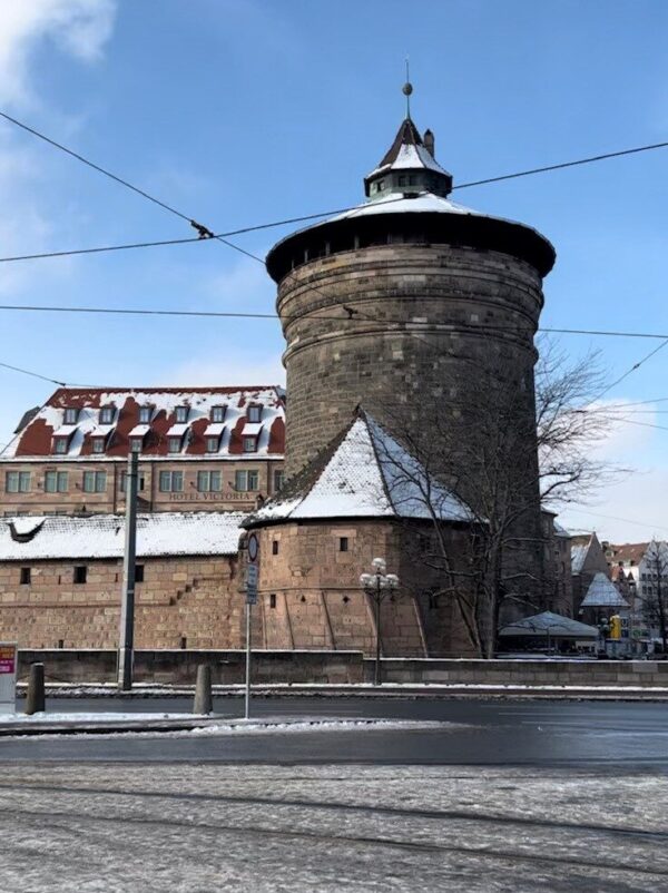 A large, medieval tower is attached to fortified city wall and is lightly dusted with snow against a blue sky