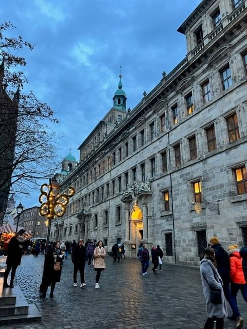 The Old Town Hall in Nuremberg is illuminated in the evening gloom, multiple windows are lit up on the old stone building.