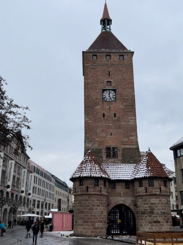 A large brick tower is standing in the middle of a city square in Nuremberg