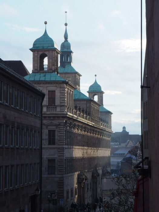 Golden rays of afternoon sunlight illuminate the green spires and domes of the Nuremberg Town Hall