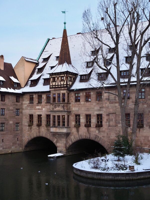 The Heilig-Geist-Spital sits over the Pegnitz sprinkled in snow during winter.