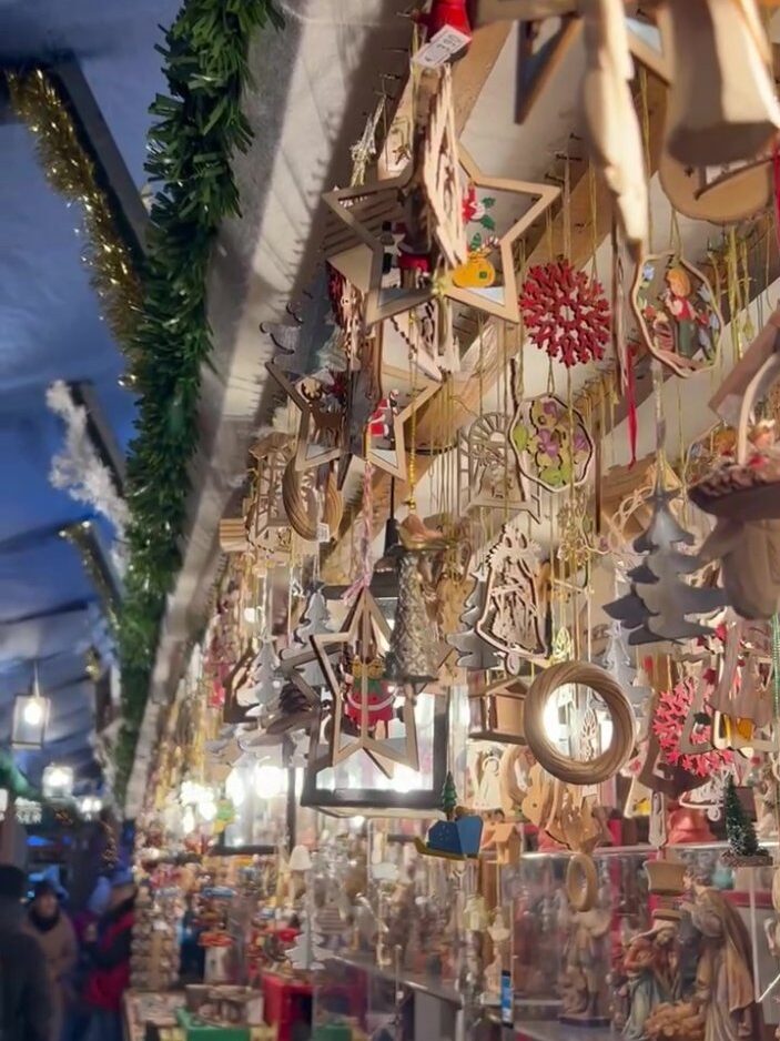 Multiple wooden Christmas tree ornaments hang from the roof of a Christmas market stall in Nuremberg, such as christmas trees and stars.