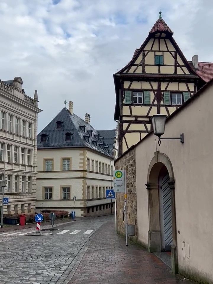 A pale yellow timber framework cottage sits atop a gently curving stone wall in the backstreets of the old town of Bamberg.