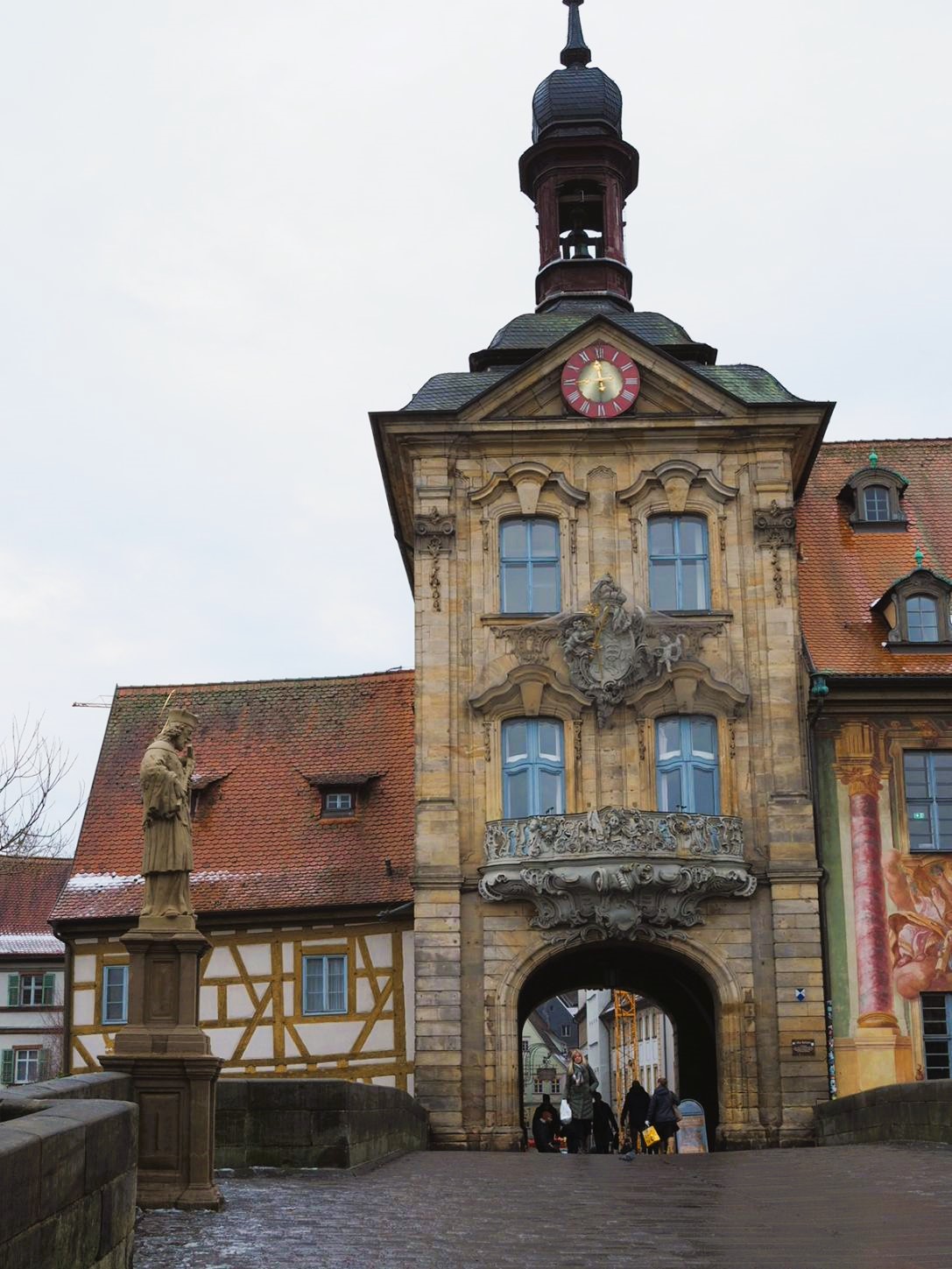 A tan statue of a religious figure stands before the Gothic Altes Rathaus, find out all about this lovely building on the ultimate walking tour & map of Bamberg, Germany.