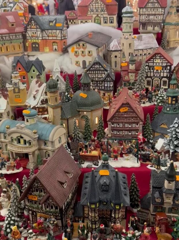 Many porcelain models of colourful half timbered houses line the shelves of a Christmas market stall, including figurines of people and snowy pine trees.