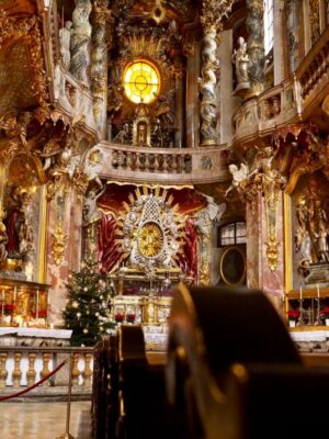 Wooden pews lead the eye to a lavishly decorated church interior of gold, rose pink marble and ornate statues, a highlight of the Munich 3 day itinerary.
