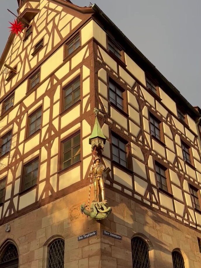 A large house made of a half timbered upper and sandstone block lower section has a statue of St. George dressed in armour and standing on a green dragon on its corner.