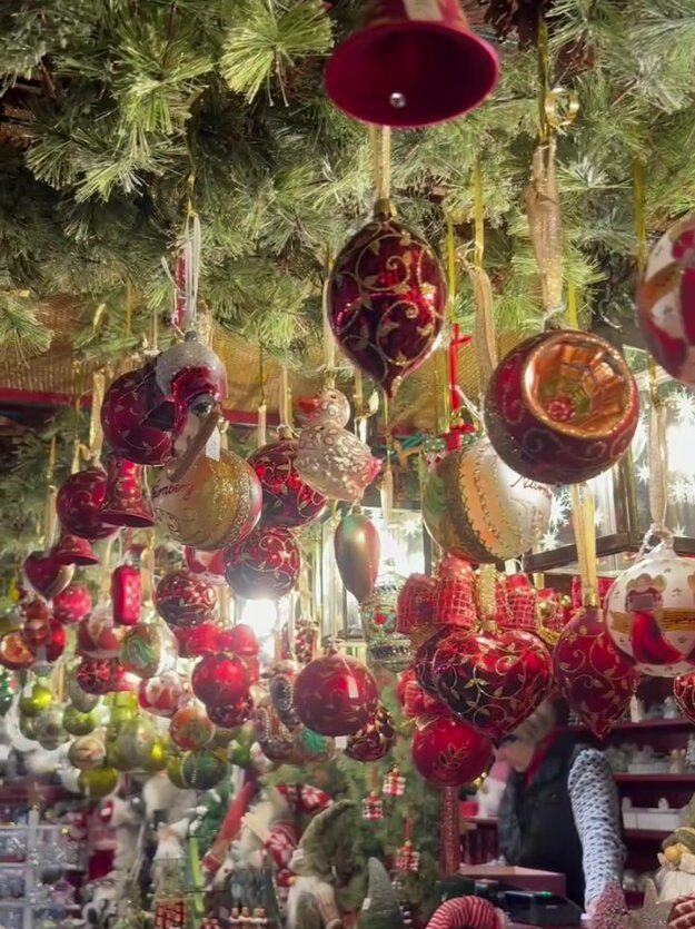 A collection of ruby and gold hued baubles hang from festive greenery at a market stall.