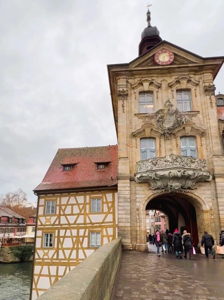 A gothic town hall constructed from sandstone straddles a pedestrian bridge, a small group of visitors in winter coats pass under the stone archway