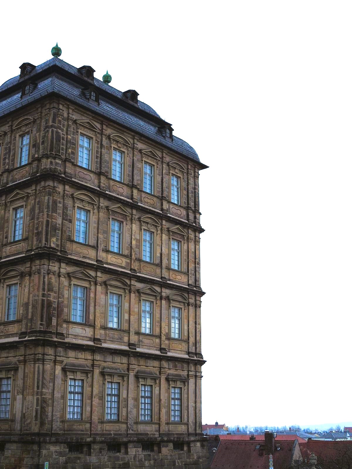 A large sandstone palace with four rows of windows stands tall over the town of Bamberg, the winter's sky reflected in the gray window panes.