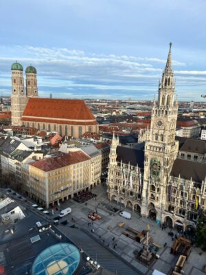 The large, red-roofed Frauenkirche with its twin onion domed towers and the Neues Rathaus with its many spires are seen from above, the square beneath is grey despite the morning light.