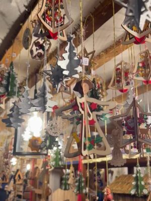 Wooden ornaments of Christmas trees and angels hang amongst lights at a market stall.