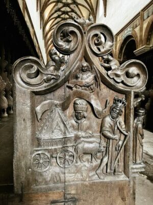 Intricate wood carvings form the end of a choir stall in the monastery church, small figures of a bishop, a king and a team of oxen dragging a cart laden with gold are all overlooked by a winged angel carved into the dark wood.