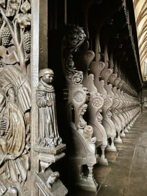 Hand carved details form visuals of a monk in his flowing cassock amidst vines and fruit, ending the row of a series of choir stalls. Large flagstones form the floor of the chapel