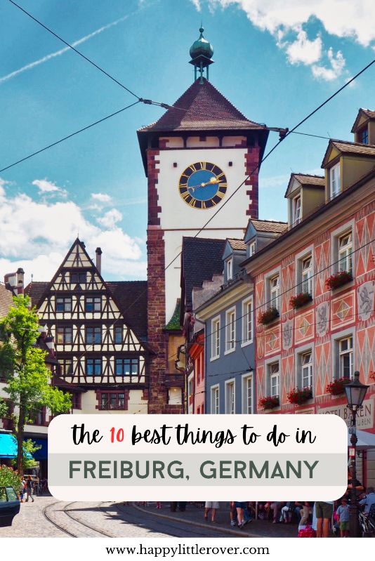 A large medieval tower made of red sandstone and white plaster with a blue clock and a half timbered house attached to the bridge stands against a blue sky with scattered cloud. The text reads the 10 best things to do in Freiburg Germany.