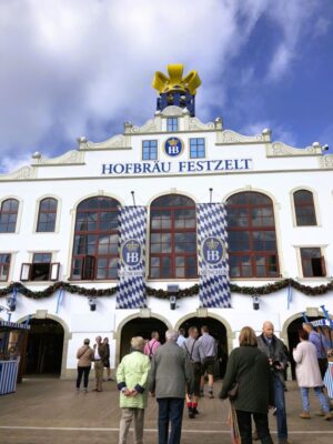 A large building hung with blue and white banners, has multiple large windows and is topped with a golden crown. You'll find more info about this tent in the guide to Oktoberfest Munich map included