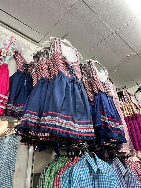 A shop interior is shown with multiple shirts and decorated dirndls hanging up on the racks in different shades.